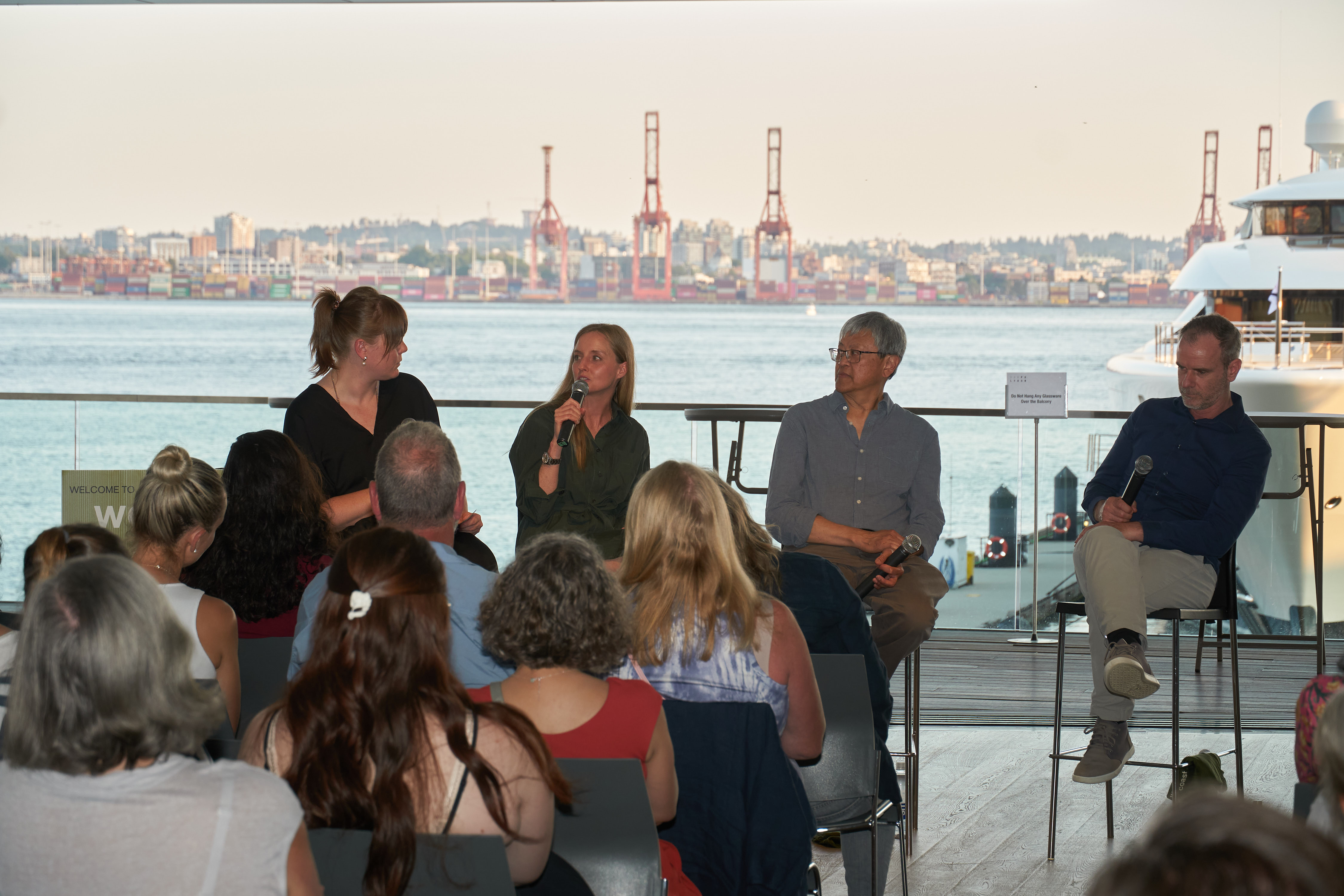 An audience listening to a panel of speakers at an outdoor event overlooking the harbour.